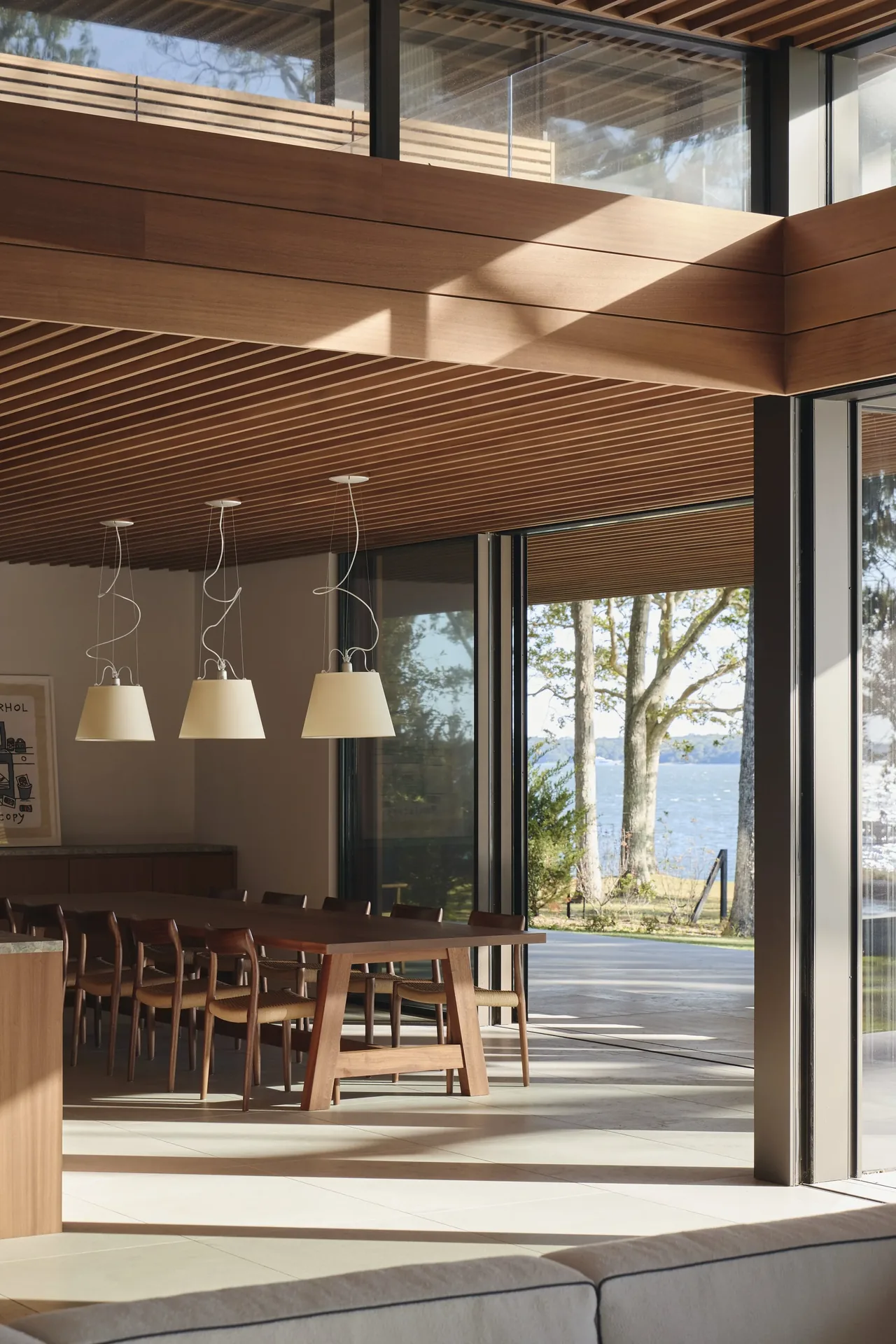 Dining area with wooden furniture and a wood slat ceiling opening to an outdoor view through large glass doors.