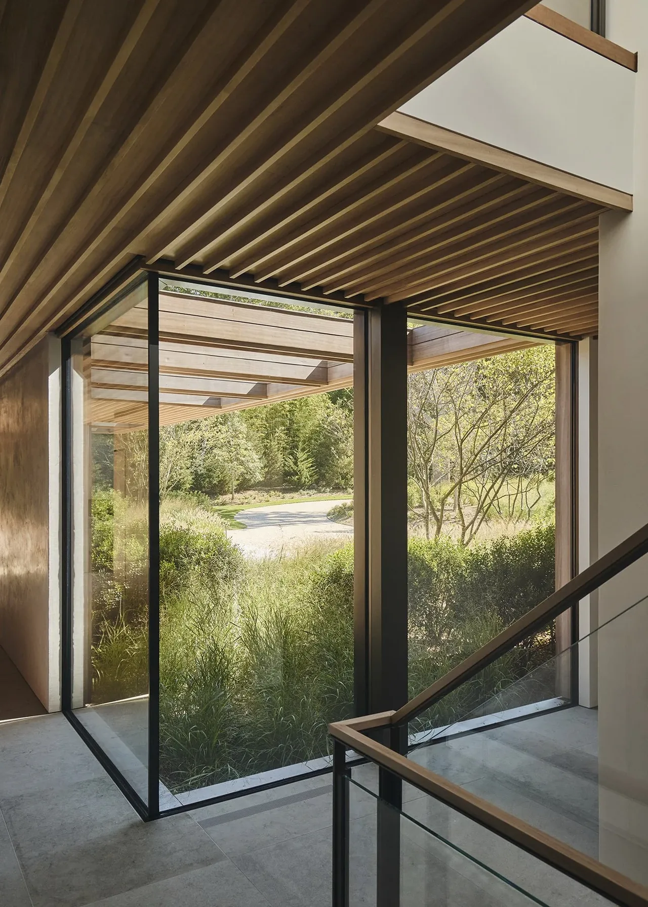 Interior view of a modern home featuring wood slat ceiling and large corner windows overlooking landscaped greenery.
