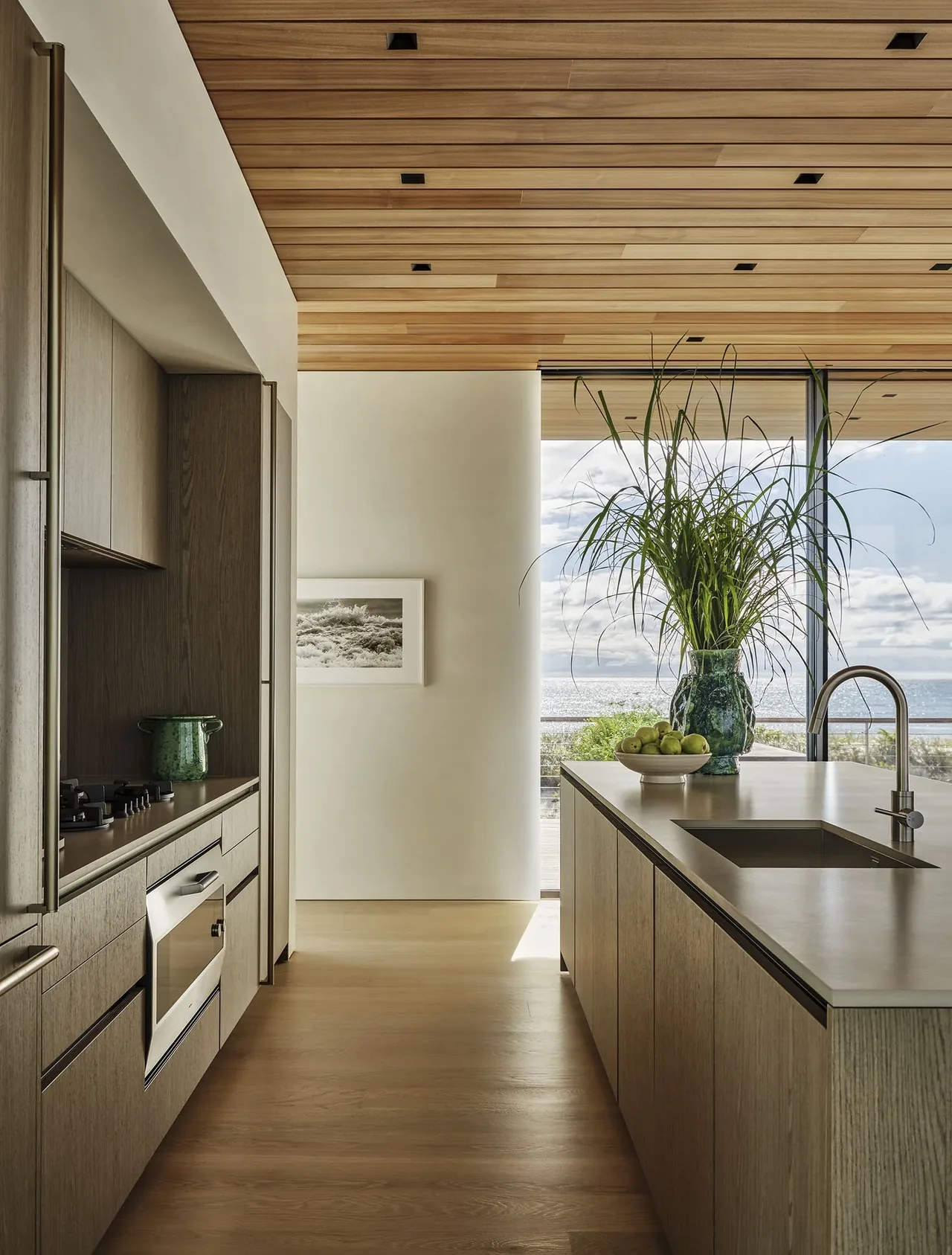 Kitchen interior with wooden ceiling and cabinetry overlooking the ocean from large windows.