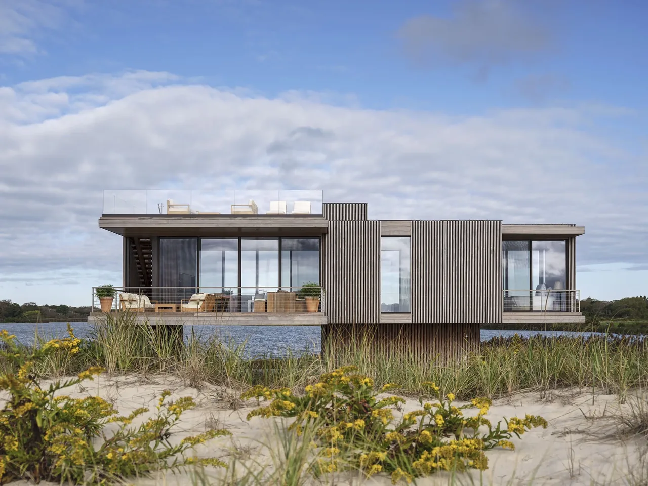 Seaside house by Stelle Architects features vertical wood siding and extensive glazing with elevated views over water.