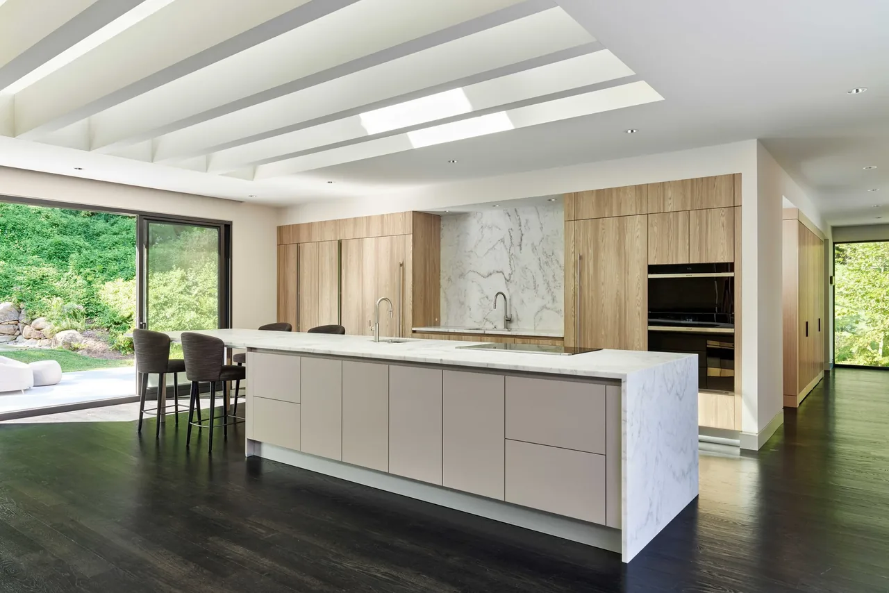 Gladwyne Residence kitchen features a marble island, light wood cabinets, and large sliding glass door to the outside.