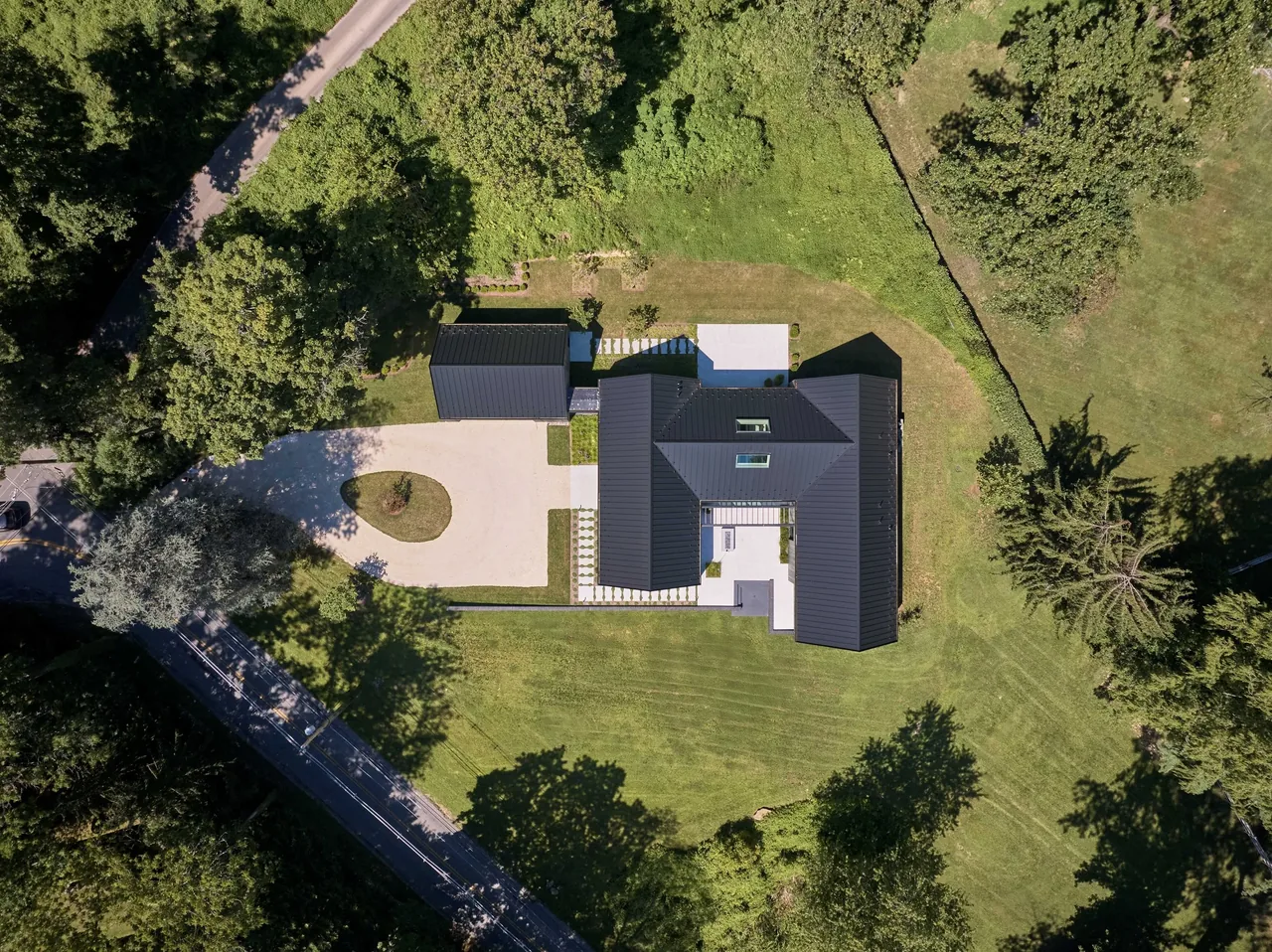 Gladwyne Residence features connected volumes with standing seam metal roofs and is set on a grassy slope.