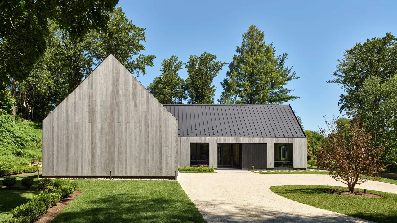 Gladwyne Residence features wood siding and a standing seam metal roof with large windows facing a grassy yard.