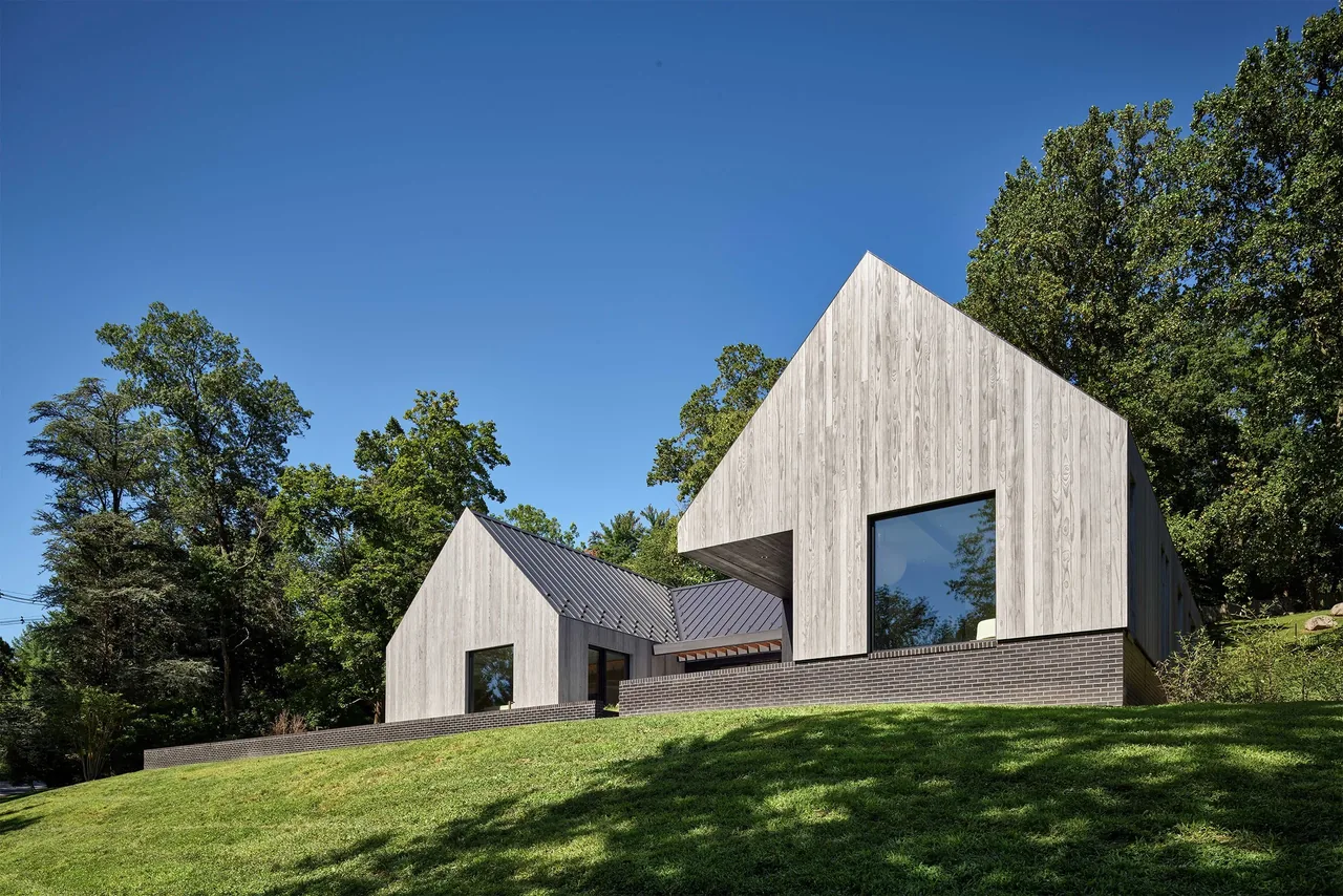 Gladwyne Residence features modern connected volumes with wood cladding and large black-framed windows.