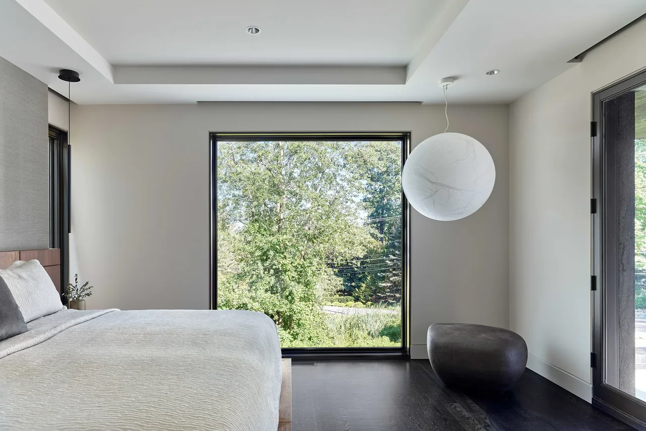 Bedroom features a large black-framed window with views of greenery, a white spherical pendant light, and dark stained wood floors.
