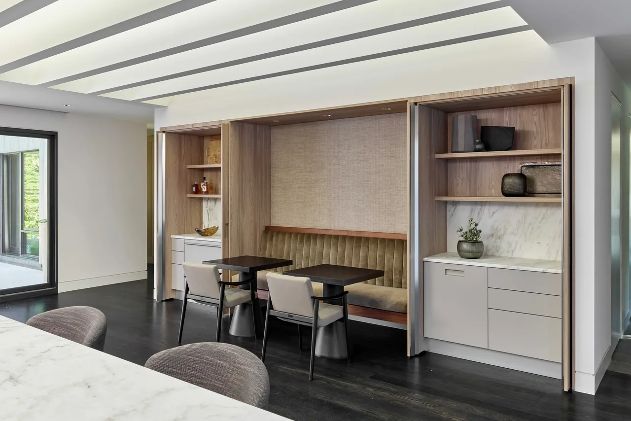 Dining nook with built-in olive-green bench seating and light wood cabinetry with marble backsplash in a modern interior.