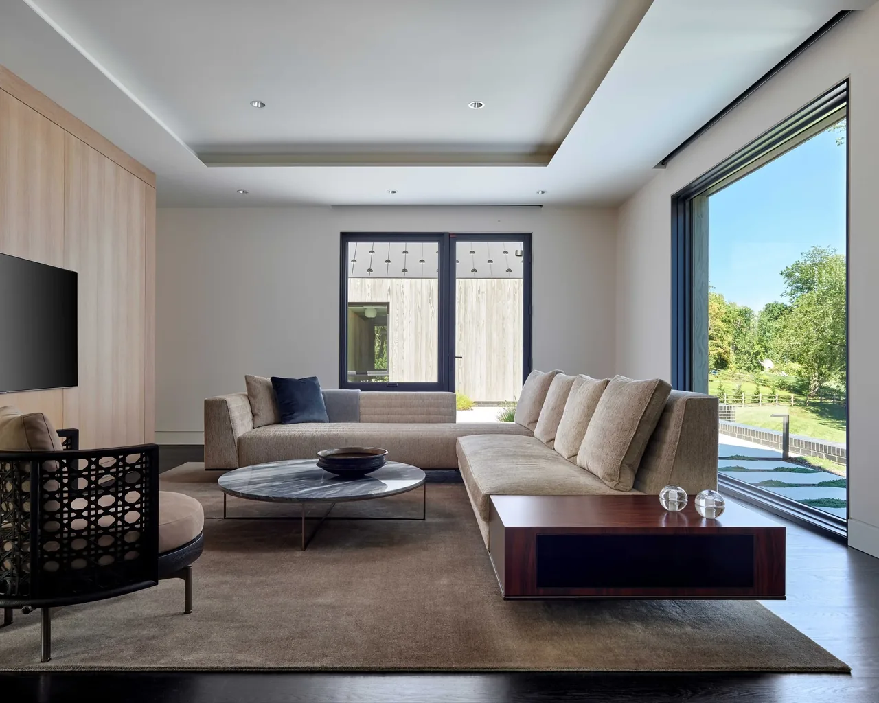 Contemporary living room with beige sectional sofa and large windows featuring black frames.