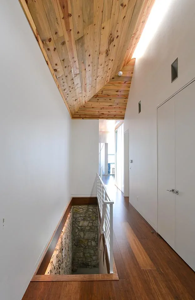 Hallway with wood plank ceiling and stone-walled stairwell in the Bottle & the Bowl project.