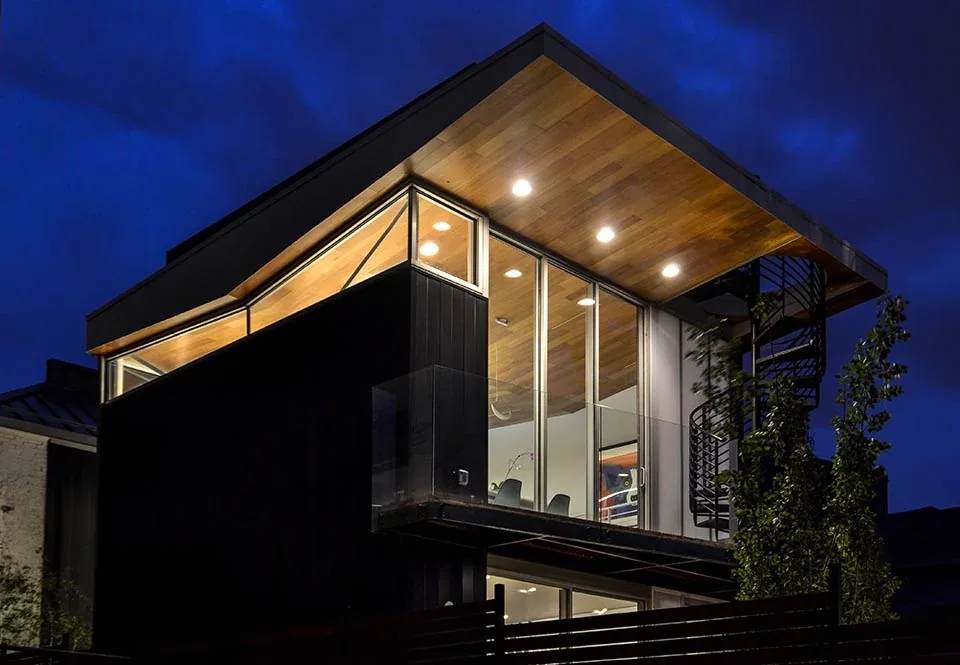 Bottle & the Bowl residence showcases a modern exterior with expansive glass walls and a wood-paneled ceiling under a flat roof.