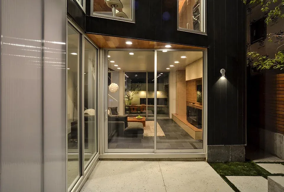 Modern living room interior seen through floor-to-ceiling sliding glass doors with outdoor patio foreground.
