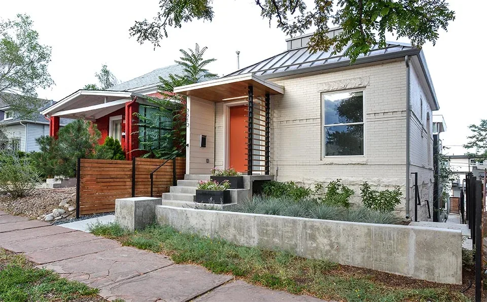The house features a painted brick exterior with a standing seam metal roof and a concrete front porch with an orange entry door.