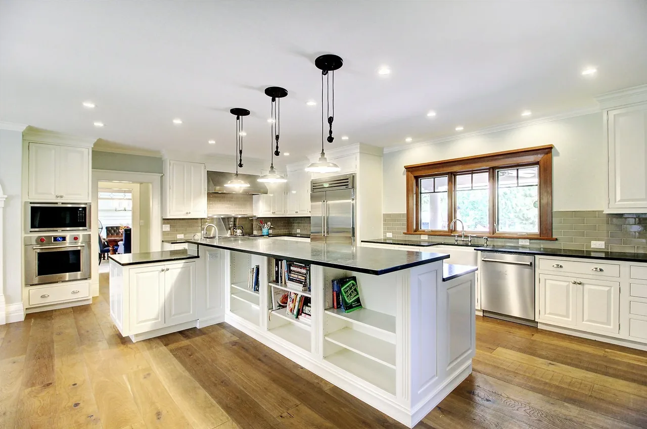 Transitional kitchen featuring a large island with built-in shelving, stainless steel appliances, and recessed and pendant lighting.