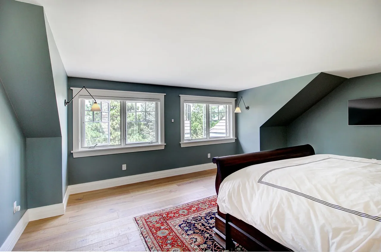 Bedroom with two windows, blue-gray walls, hardwood floors, and traditional dark wood bed frame.
