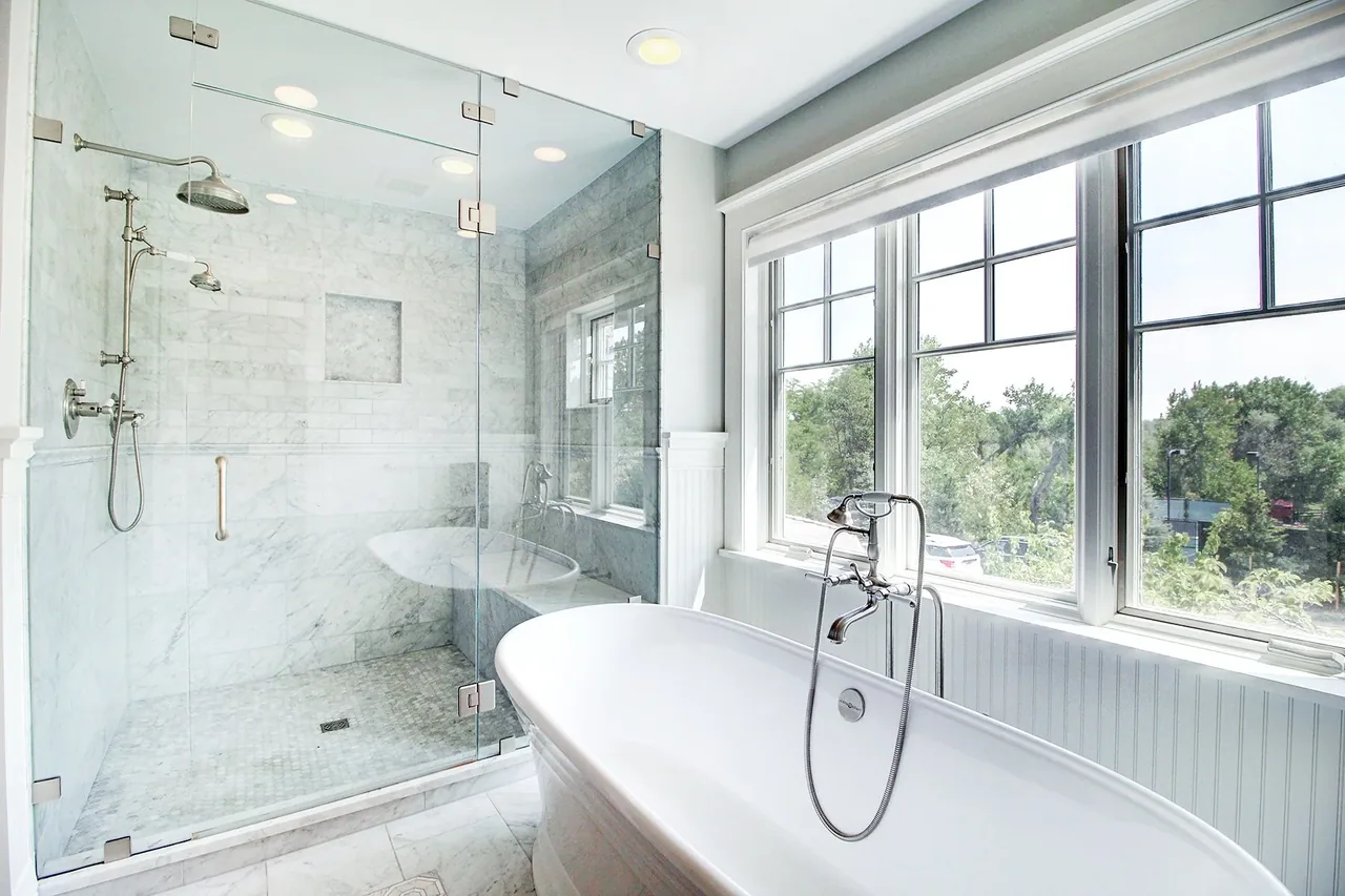 Bathroom features a freestanding tub, large divided lite windows, and a glass shower with marble tile in a transitional remodel.