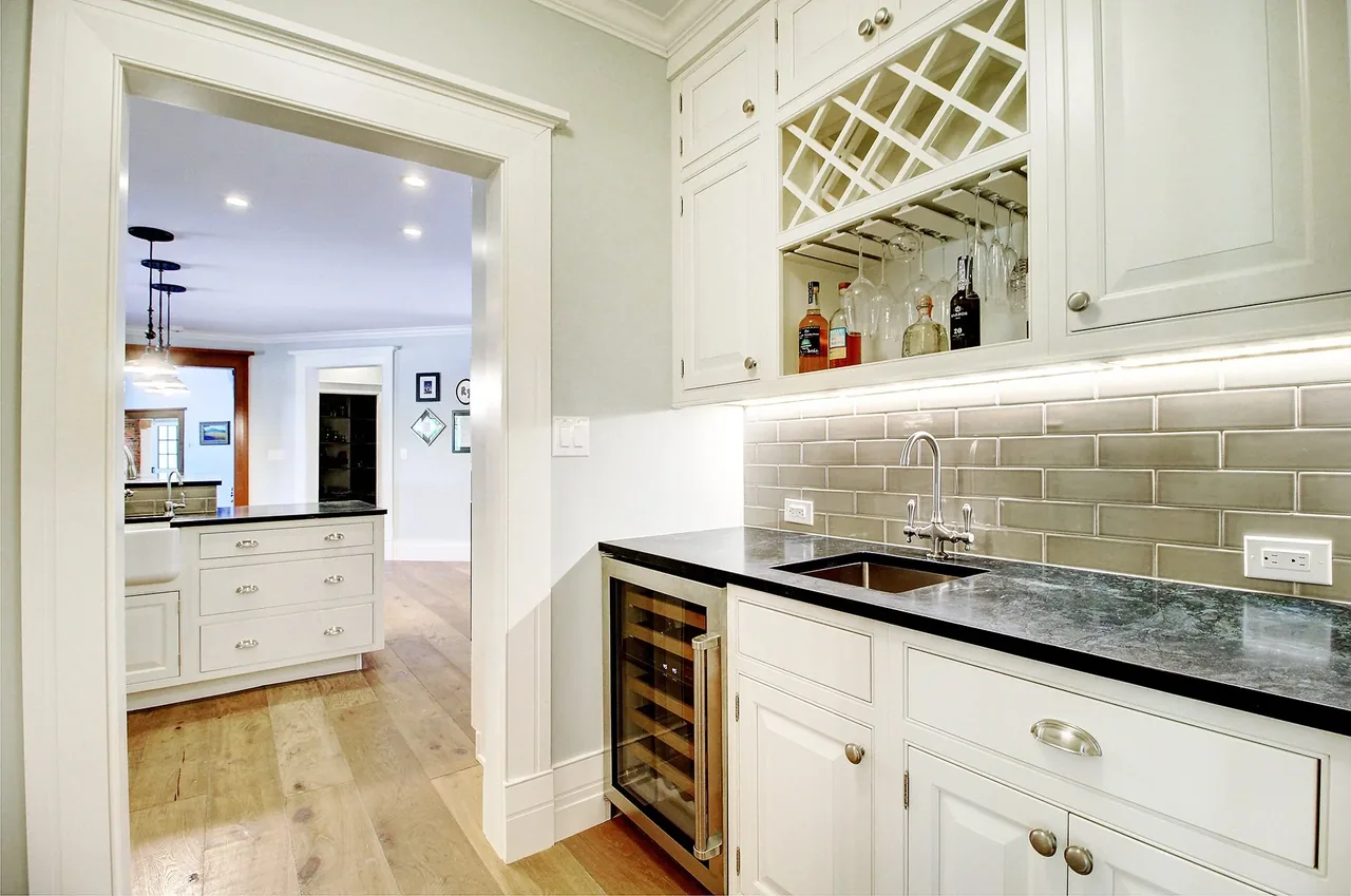 Kitchen area in the Transitional Country Remodel with black countertops and white cabinetry featuring a built-in wine rack and glass storage.