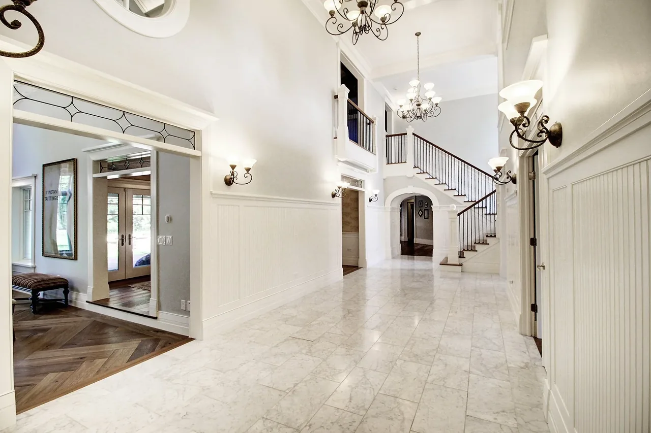 Transitional country style hallway with white marble tile flooring and wrought iron railings with multiple light fixtures.