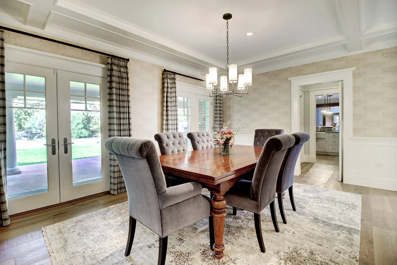 Dining room features a wooden table with six gray tufted chairs and a pendant chandelier above.