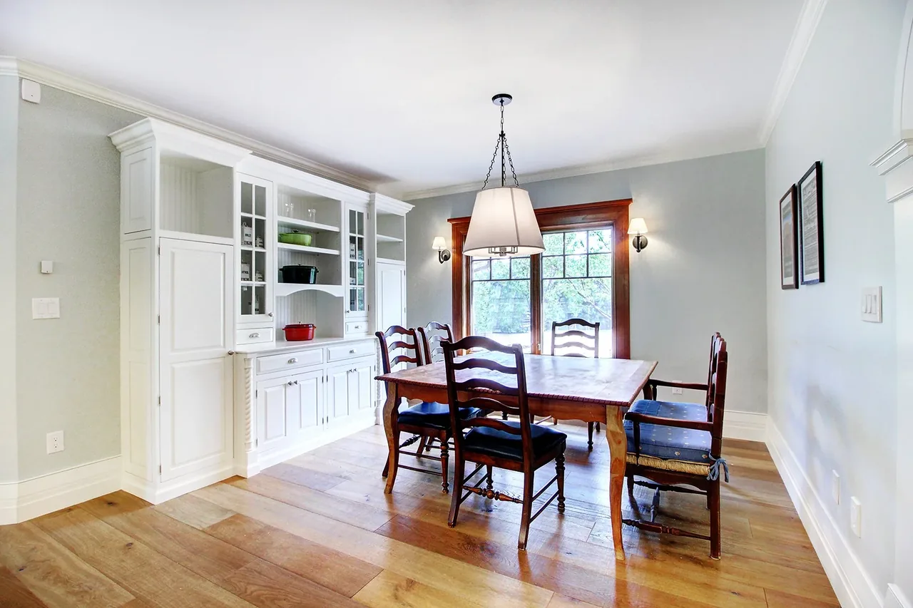 Dining room features a wooden table with six chairs and built-in white cabinetry next to a large wood-trimmed window.