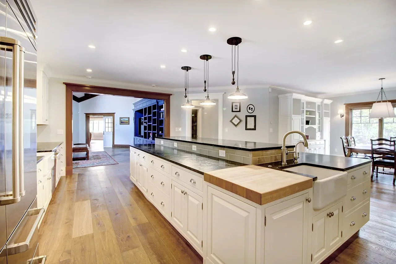 Open kitchen with large island, farmhouse sink, and pendant lighting opens to dining area and living space with built-in shelves.