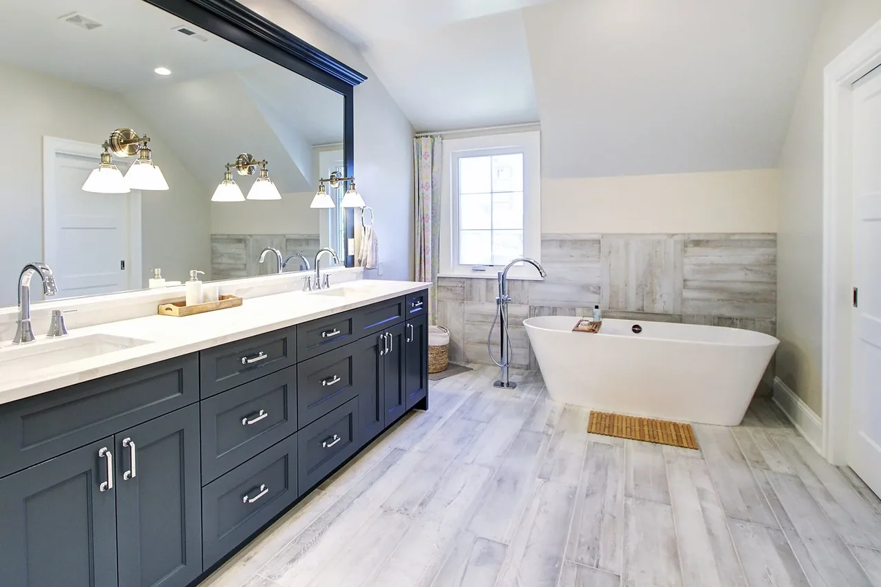 Blue cabinet double vanity with undermount sinks and a freestanding tub in a light wood-tile bathroom.