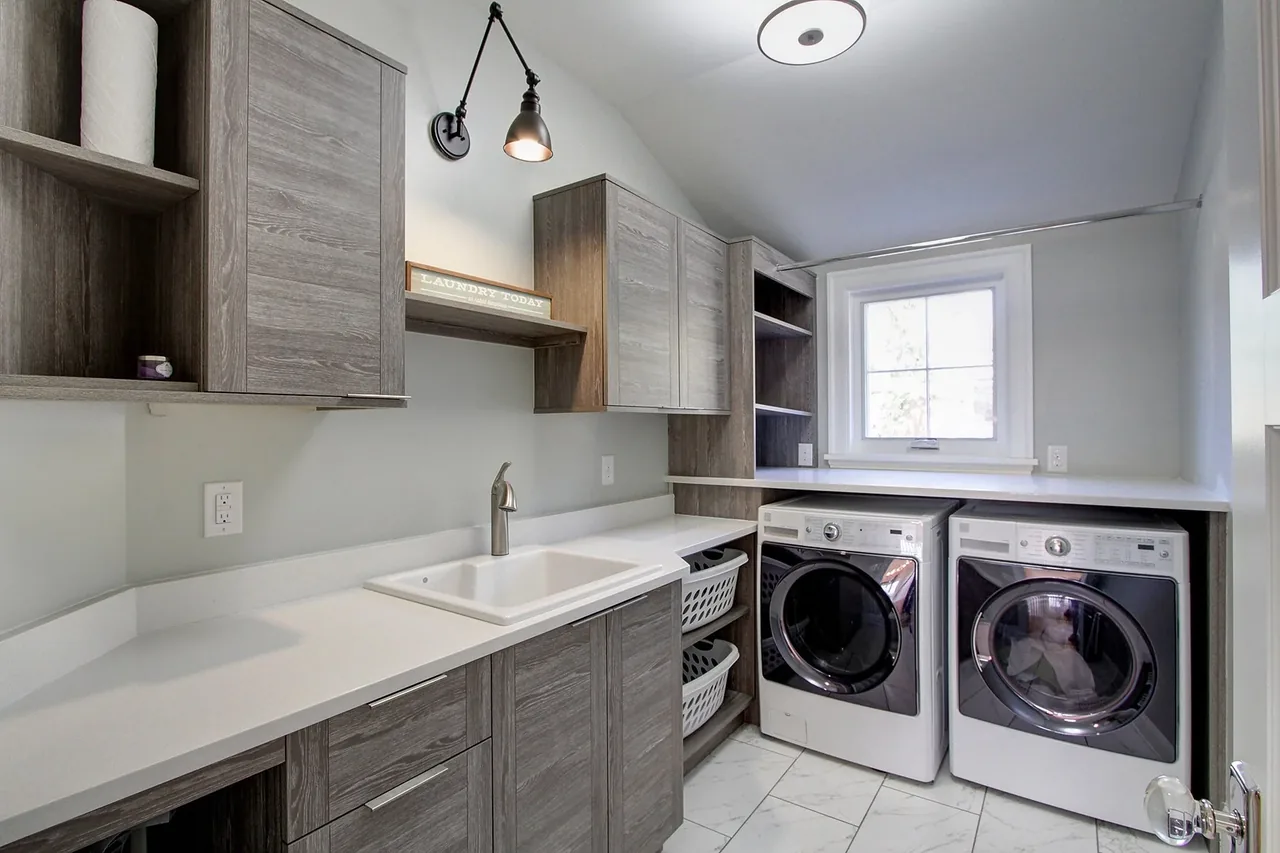 Laundry room featuring gray wood cabinets, a white sink, and front-loading washer and dryer beneath a window.