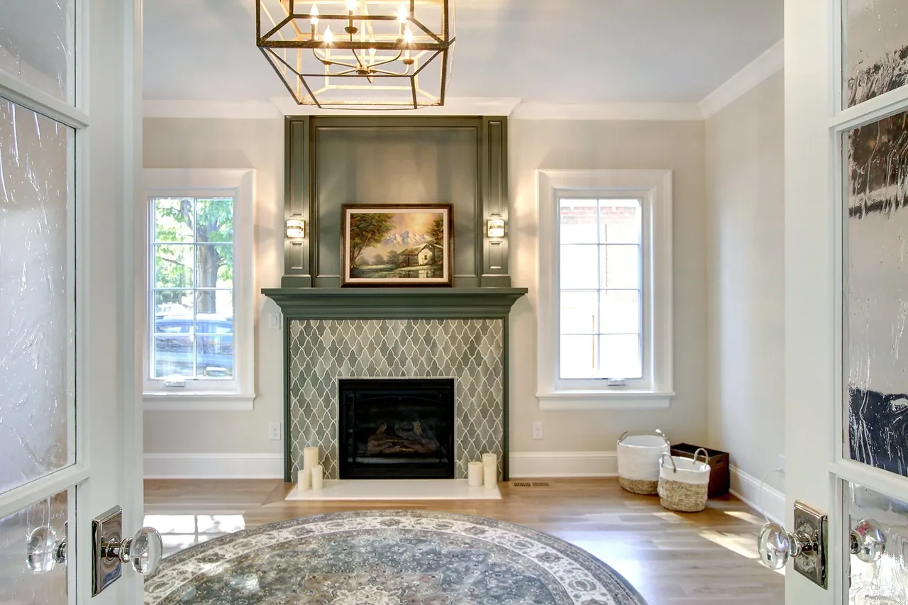 Living room features a fireplace with patterned tile surround and green mantel, flanked by two windows and a decorative round rug.