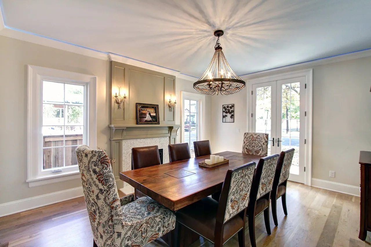 Dining room featuring a wooden table for eight, a chandelier, fireplace, and double doors to the exterior.