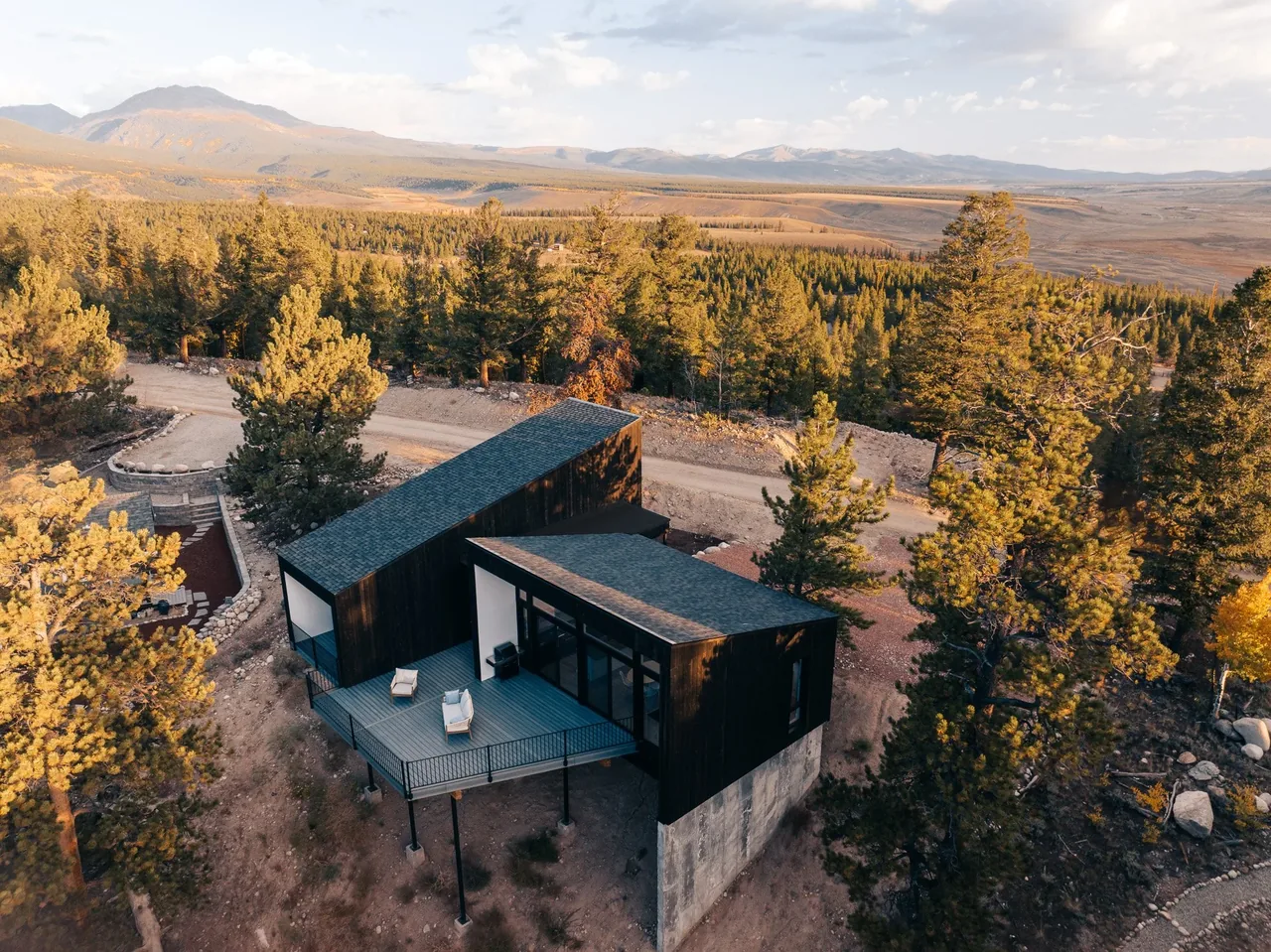 Twin Lakes Bothy features dark wood siding with an elevated deck and concrete foundation, situated in a natural hillside setting.