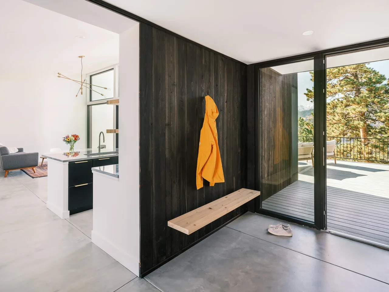 Entry area features black wood paneling, a floating bench, and floor-to-ceiling glass sliding doors opening to an elevated deck with mountain views.