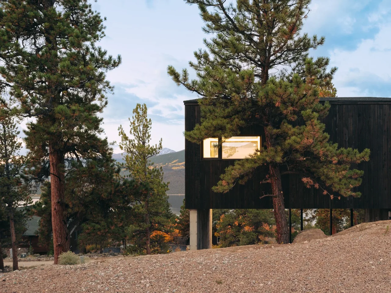 Twin Lakes Bothy features a dark wood exterior elevated above sloped terrain with mountain views.