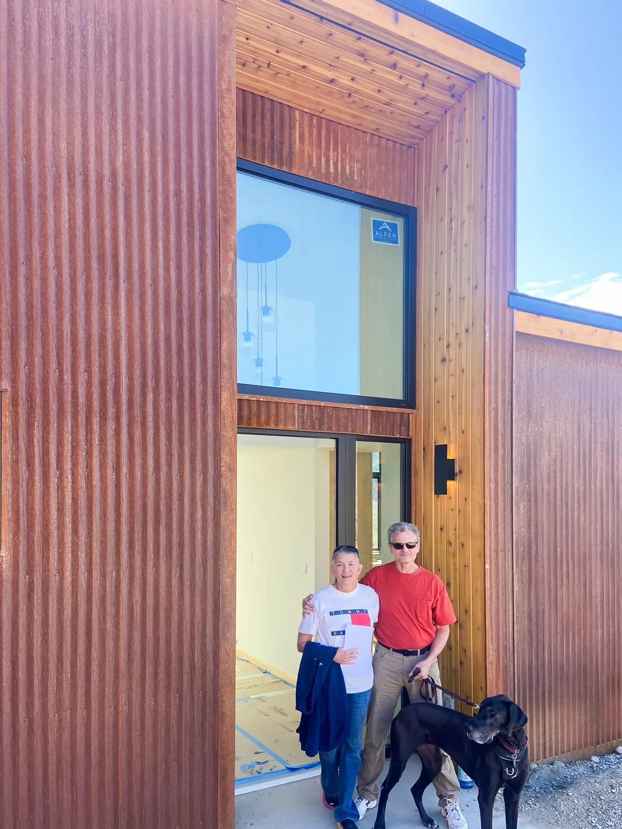 Entrance of a modern house featuring rust-colored corrugated metal siding, wood detailing, and large black-framed windows.