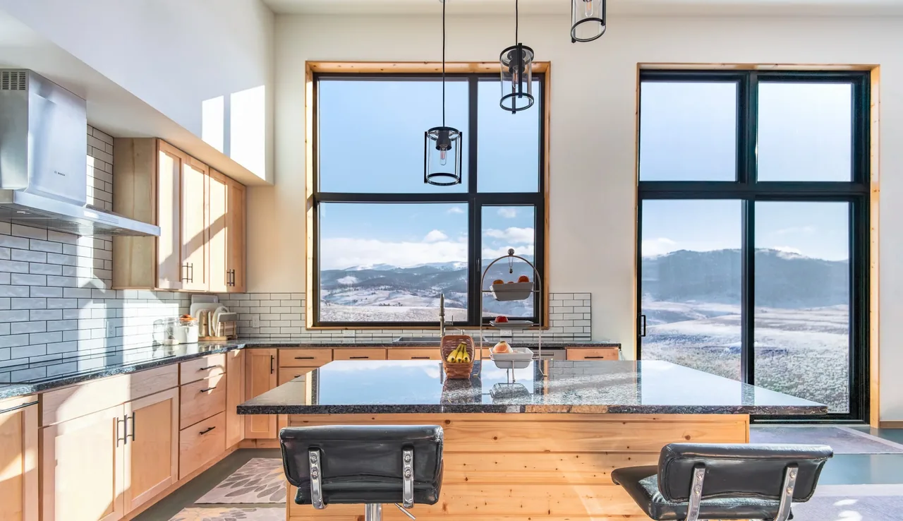 The Blue J project kitchen features large black-framed windows with scenic mountain views and a central island with seating.