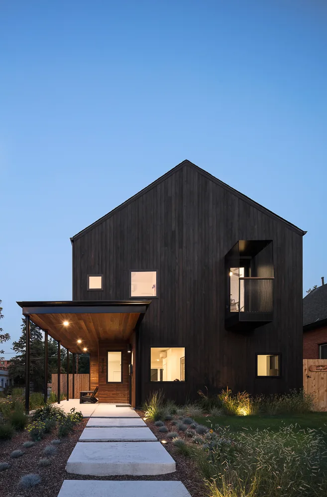 The 43rd Residence features dark vertical wood siding, small square windows, a covered porch, and a projecting upper-story balcony.