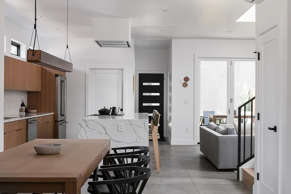 View of a modern kitchen with wooden cabinets and a dining area with black chairs at a wooden table.