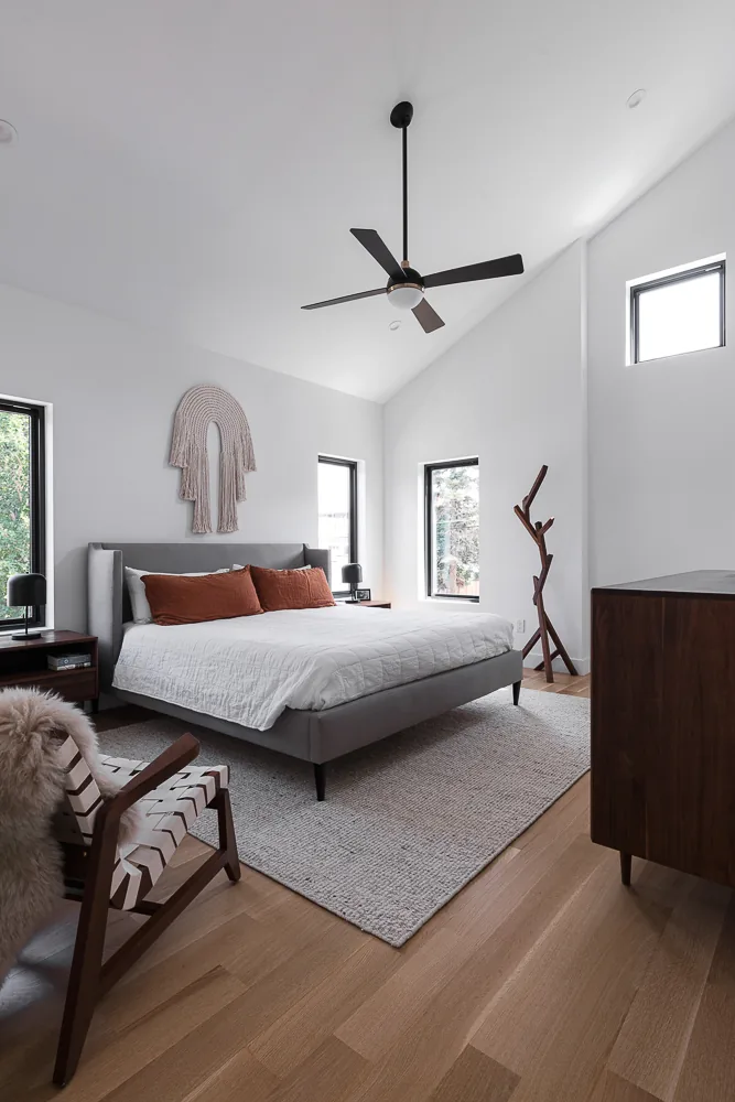 Bedroom in 43rd Residence with vaulted ceiling and black window frames, featuring a gray bed and wooden furniture.
