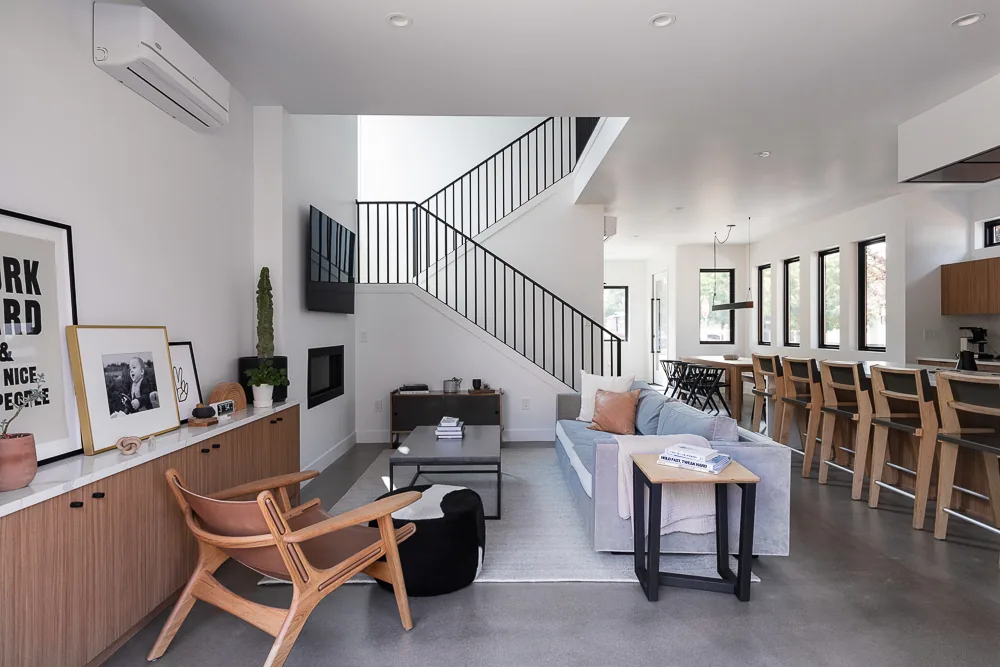 Open plan living and kitchen space with black window frames, wooden cabinetry, and staircase with black metal railing.