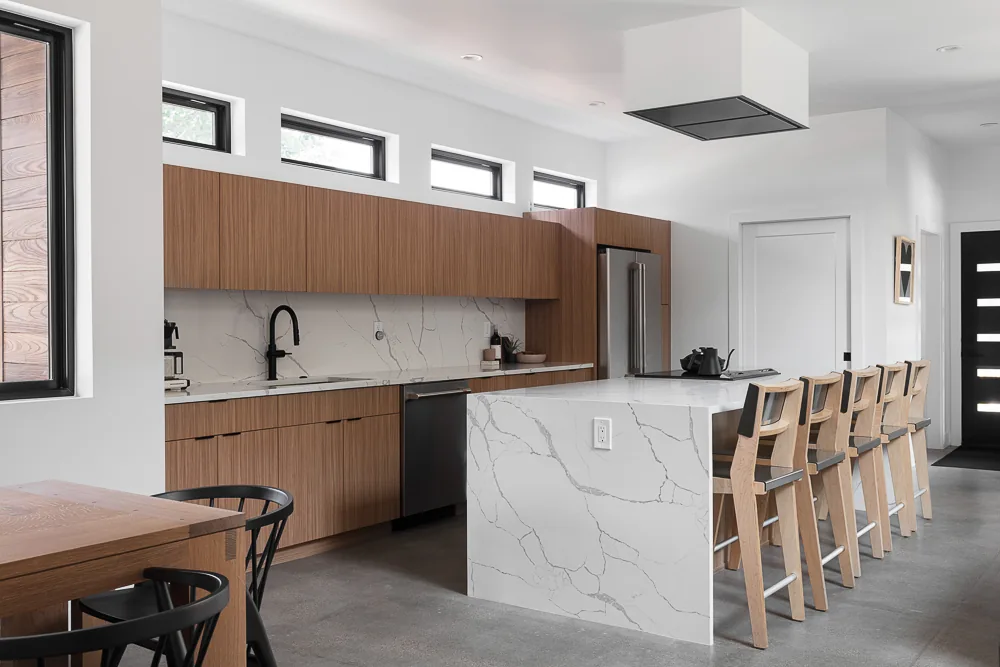 Kitchen features a marble island and wood cabinetry with black faucet and small rectangular clerestory windows for natural light.