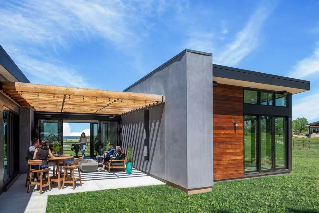 Outdoor living space with wooden pergola, metal railings, and large glass doors at Hoff Residence by UNUM Collaborative.