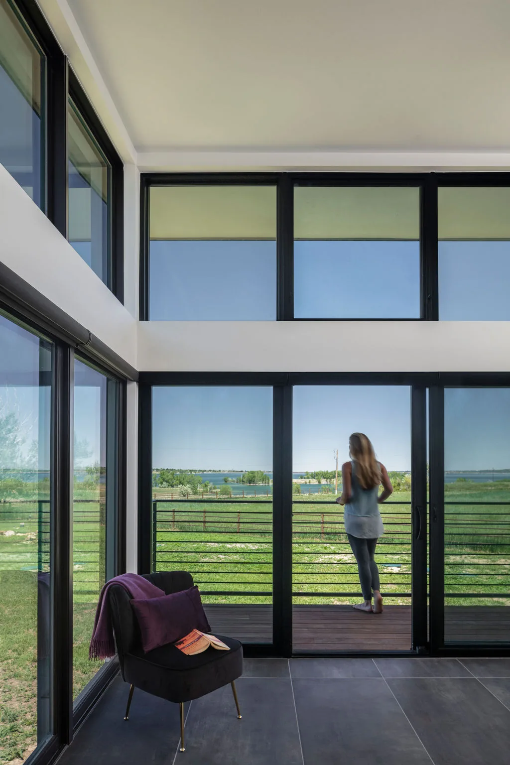 Hoff Residence interior space features large black-framed windows looking onto a deck and open green landscape with water beyond.