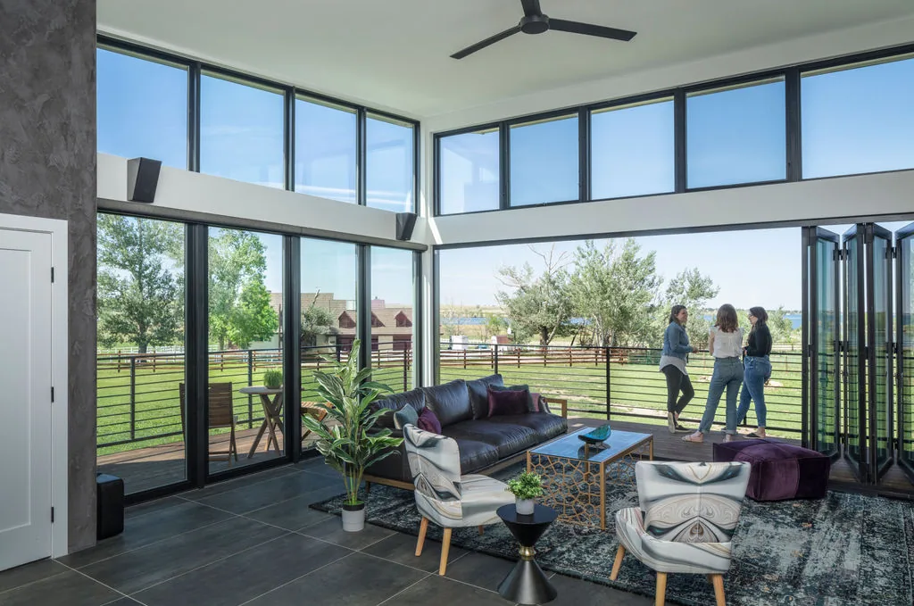 Living area featuring floor-to-ceiling corner windows, sliding glass doors, and access to a balcony with outdoor seating and metal railing.