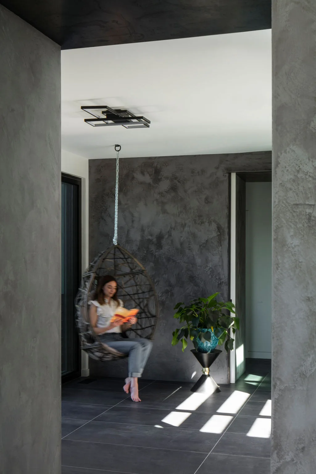 Interior space features a hanging egg chair, textured gray wall finish, and large tiled floor.