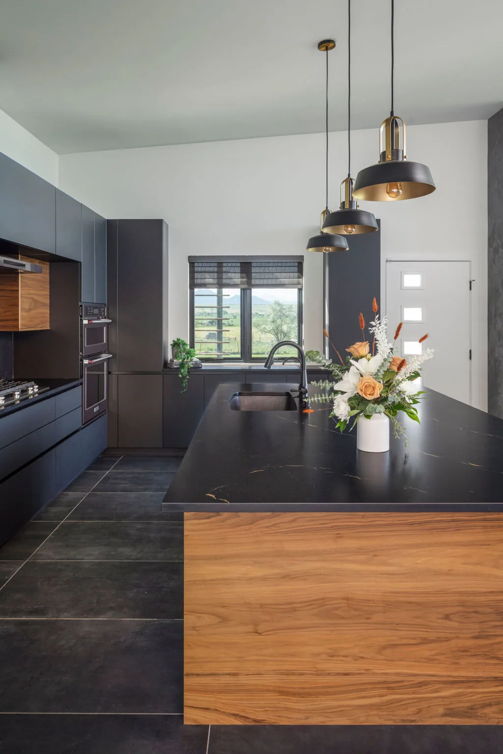 Hoff Residence kitchen features sleek black cabinets, a wood-paneled island, and modern pendant lighting.