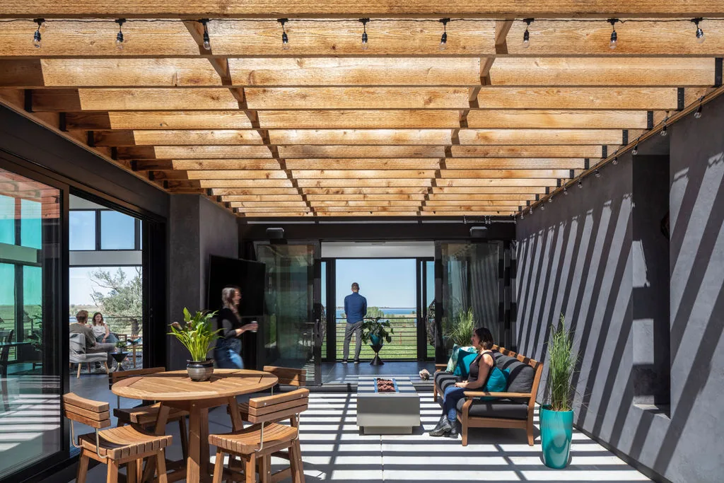 The Hoff Residence features a covered patio with a wooden pergola creating a pattern of shadows on the outdoor seating area.