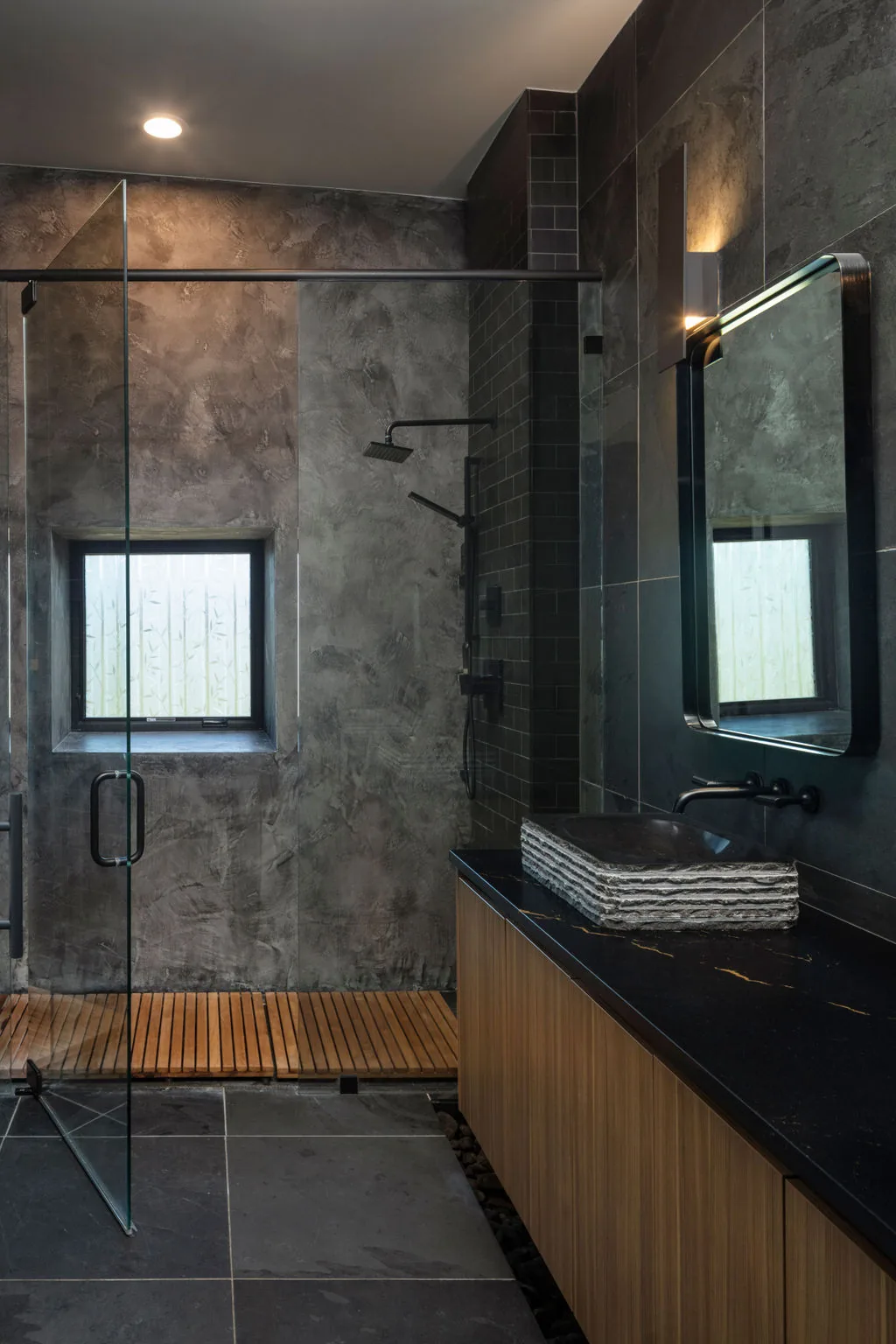 Bathroom featuring textured concrete-look walls, a frameless glass shower, and a wood vanity with a stone vessel sink.