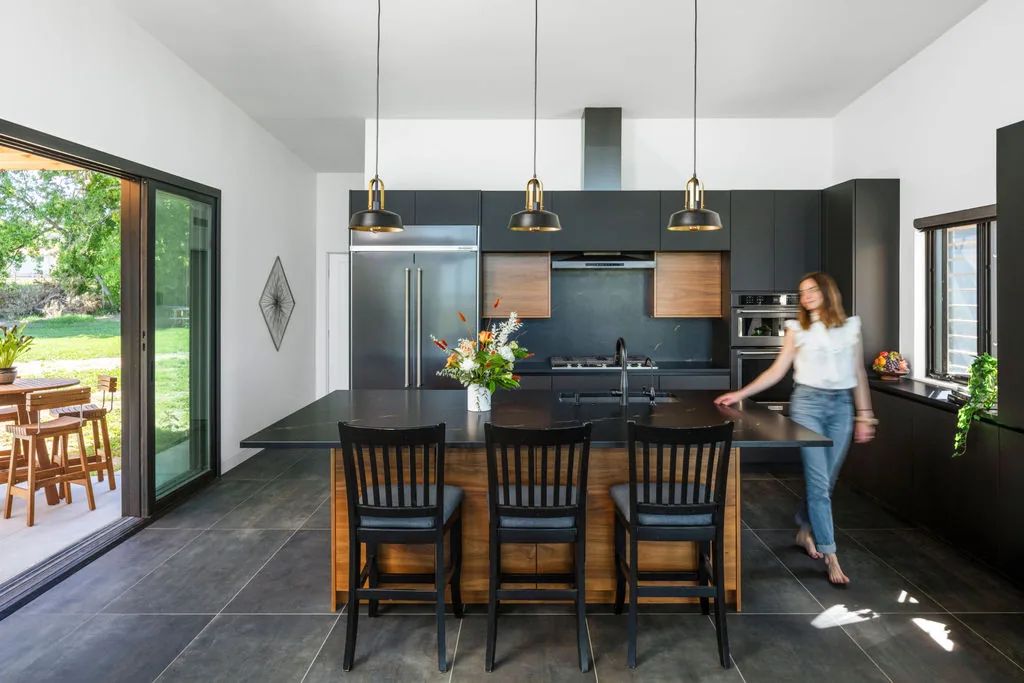 Kitchen in Hoff Residence features black cabinets, a large island with black countertop, and sliding glass doors opening to outdoor dining.
