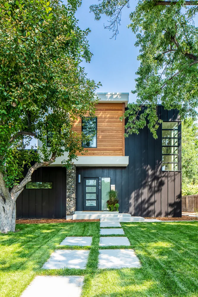 Dempster Residence features black vertical metal siding, wood cladding, and a gabion stone pillar at the entrance.