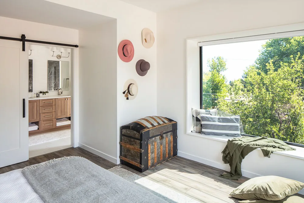 Bedroom corner features a large picture window with seating, an antique trunk, and a view of lush greenery outside.