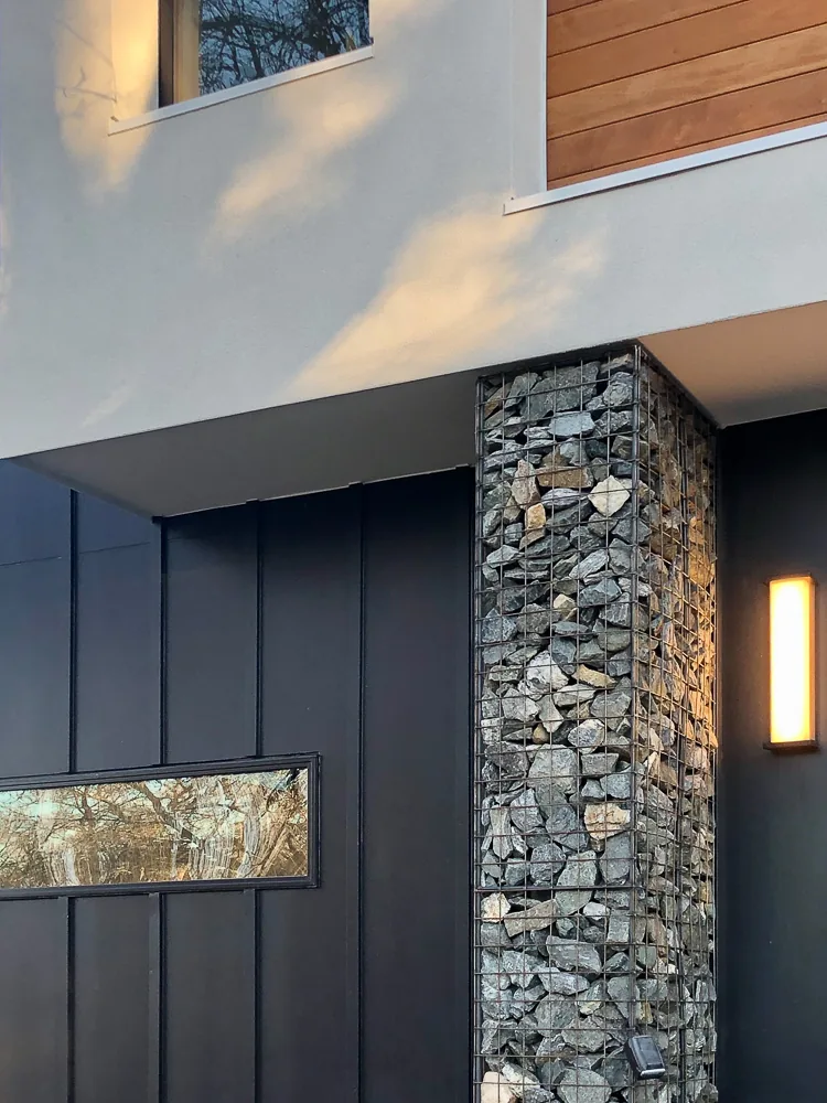 Detail of the Dempster Residence's exterior showing metal panel siding, a gabion stone pillar, and a horizontal window.