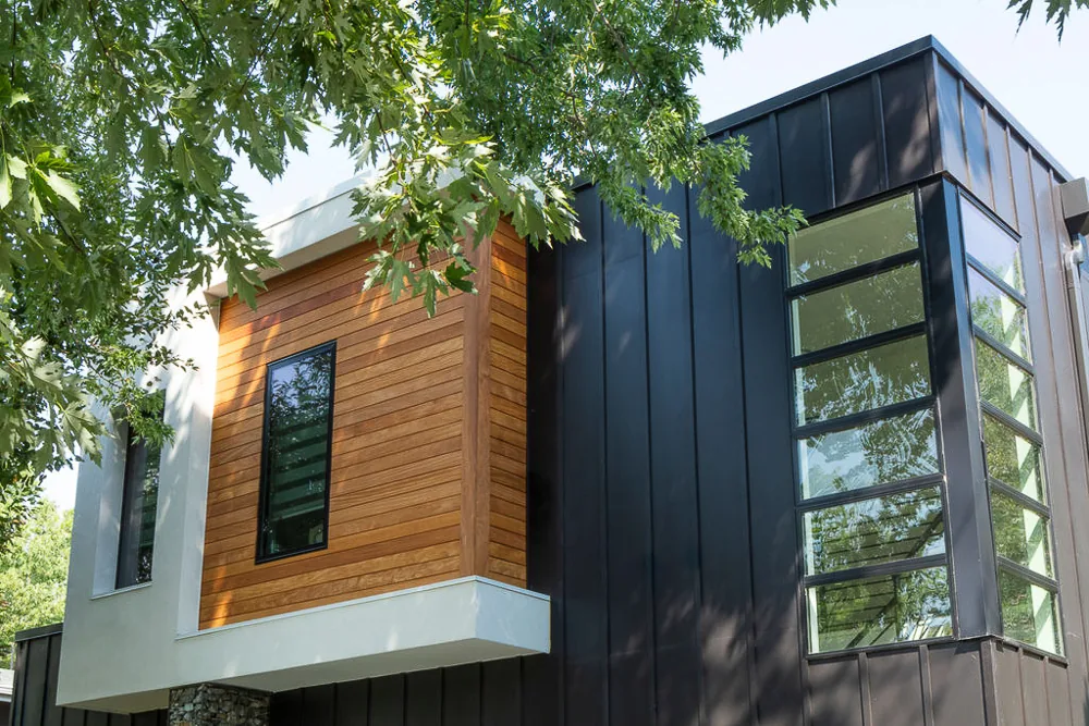 View of a modern residential building with black and wood siding partially framed by tree branches.