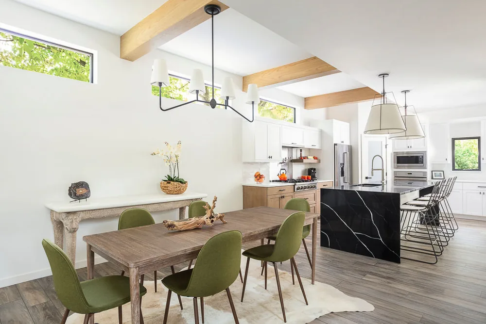 Dining area with wood table and green chairs opens to kitchen with black marble island, white cabinetry, and wood accents.